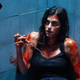 A dark-haired woman with blood smeared on her arms, face, and chest sits in a shower holding a knife in a scene from horror film The Advent Calendar.